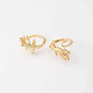 Peut inclure: Deux bagues dorées, chacune ornée d'un motif de lézard détaillé. Les lézards sont sculptés avec des écailles et des pattes complexes. Les bagues sont posées sur un fond blanc. Ce sont des bijoux uniques.