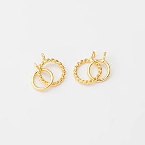 Könnte beinhalten: Zwei goldfarbene Ohrringe. Jeder Ohrring hat einen kleinen, glatten Kreis, der mit einem größeren, gedrehten, seilartigen Kreis verbunden ist. Die Ohrringe haben oben eine kleine Schlaufe zum Befestigen. Der Hintergrund ist schlicht weiß.