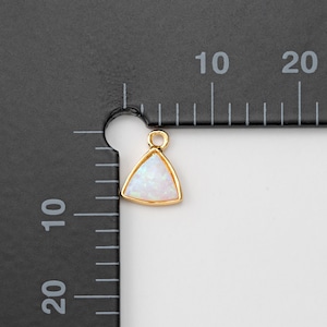 May include: Gold triangle charm with a white opal gemstone. The charm is about 1 cm in size.