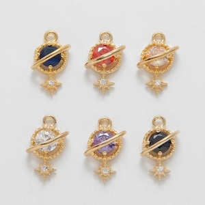 May include: Six gold-colored planet charms with colorful gemstone centers. Each charm features a ring around the gemstone and a star-shaped accent below. The gemstones are in various colors, including blue, red, clear, white, purple, and black.