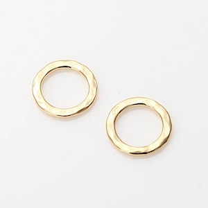 以下が含まれることがあります： 金色のハンマー加工が施された2つの金属リング。リングは円形で、表面はテクスチャ加工、中央は滑らかで開いています。リングは白い背景に表示されています。