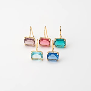 May include: Five pairs of gold-colored earrings with rectangular, colorful gemstones. The gemstones are in shades of pink, red, teal, blue, and light blue. The earrings are displayed on a white background.