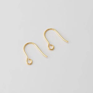 May include: Two gold-colored earring hooks are displayed against a white background. The hooks are curved, with a small loop at the bottom and a longer, pointed top. The hooks are made of a shiny, metallic material.