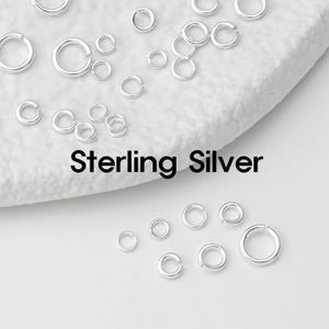 Pode incluir: Uma coleção de argolas de prata esterlina de vários tamanhos espalhadas em uma superfície branca. O texto "Sterling Silver" é exibido em preto abaixo. Os anéis são brilhantes e brilhantes.