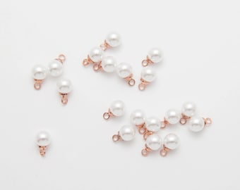 May include: A selection of white faux pearl beads with rose gold-coloured metal findings. The beads are round and have a glossy finish. Some are linked in pairs or trios, others are single.