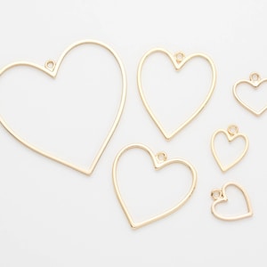 May include: Five gold-colored metal heart-shaped frames of varying sizes. The frames have a loop at the top for hanging.