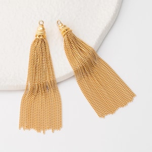 Puede incluir: Dos borlas de cadena dorada con adornos decorativos. Las borlas están hechas de muchos hilos de pequeñas cadenas unidas, creando un efecto fluido y con flecos. Las partes superiores tienen un pequeño lazo para colgar.