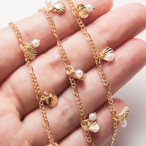 Könnte beinhalten: Eine goldene Kettenkette mit mehreren kleinen Perlen- und Muschel-Anhängern. Die Kette liegt auf einer Hand.