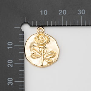 May include: Gold-toned metal charm featuring a raised design of a single rose with leaves. The charm is approximately 2 cm in diameter.