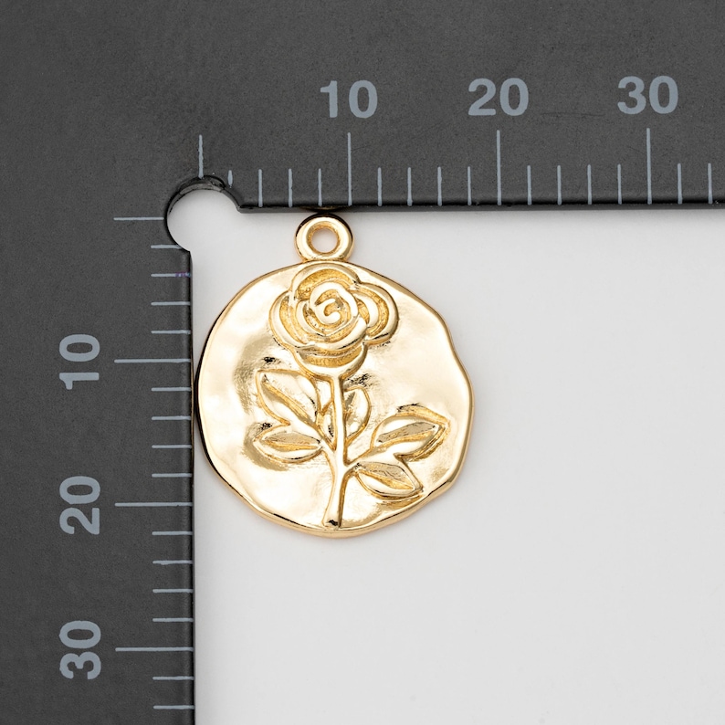 May include: Gold-toned metal charm featuring a raised design of a single rose with leaves. The charm is approximately 2 cm in diameter.