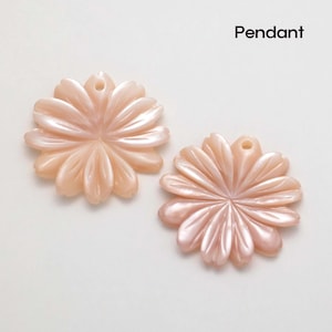 Puede incluir: Dos colgantes con forma de flor en color melocot&oacute;n suave. Cada colgante tiene un agujero en la parte superior para ensartar. Los p&eacute;talos est&aacute;n tallados con un brillo sutil y nacarado. La palabra "Colgante" est&aacute; escrita en negro.
