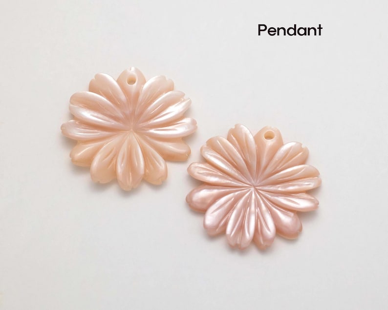 Puede incluir: Dos colgantes con forma de flor en color melocot&oacute;n suave. Cada colgante tiene un agujero en la parte superior para ensartar. Los p&eacute;talos est&aacute;n tallados con un brillo sutil y nacarado. La palabra "Colgante" est&aacute; escrita en negro.
