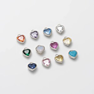 May include: Assortment of 12 heart-shaped charms with different colored crystal stones. The charms are silver-toned and have a loop for attaching to a necklace or bracelet.