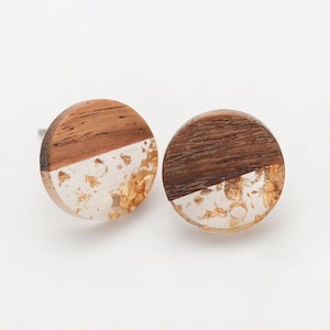 May include: A pair of circular stud earrings. Each earring features a half-wood, half-resin design. The wood is a natural brown, and the resin contains gold leaf. Set against a white backdrop.