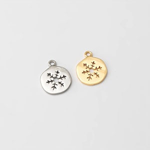 May include: Two snowflake charms. One is silver-colored, the other is gold-colored. Both charms have a circular shape with a snowflake design cut out in the center. The charms have a small loop at the top for attaching to a chain or other jewelry.