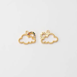 May include: Two gold-coloured cloud charms with a beaded edge. One charm features a rainbow of colourful gemstones. Each charm has a small loop at the top for attaching to jewellery. The charms are on a white background.
