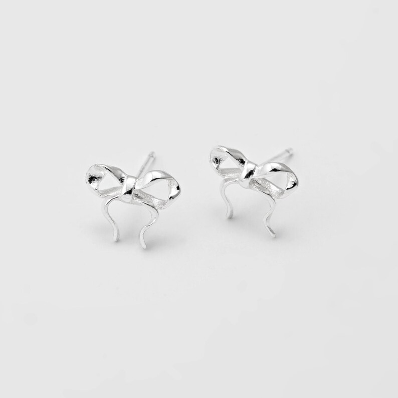 Op de afbeelding: Een paar zilveren oorbelletjes in de vorm van een strik.