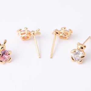 May include: Four gold-colored stud earrings. Two pairs feature a gold-colored animal design, one a bunny with a pink gem, the other a teddy bear with a clear gem. The other two pairs are a gold-colored butterfly design with a pink gem.
