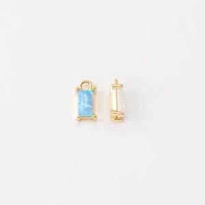May include: Two gold-toned charms with a rectangular opal stone. The charm on the left has a light blue opal, and the charm on the right has a white opal.