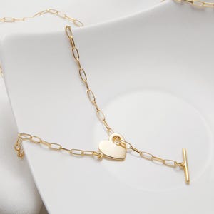 May include: A gold chain necklace with a heart-shaped pendant and a t-bar clasp.