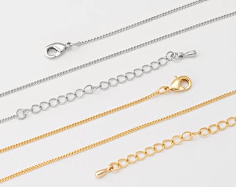 May include: Close-up of several silver and gold-coloured chain necklaces with lobster claw clasps and extender chains. The chains are displayed against a white background, showcasing their delicate designs and varying lengths.