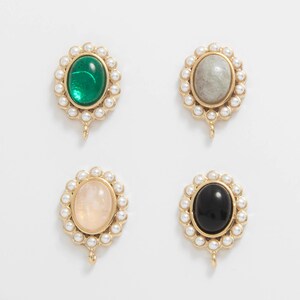 May include: Four gold-toned pendants with oval-shaped gemstones in green, gray, peach, and black. Each gemstone is surrounded by small, white pearls. The pendants have a small loop at the bottom for attachment.