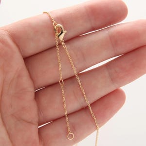 Op de afbeelding: Een gouden ketting met een karabijn sluiting en een springring. De ketting is delicaat en heeft een fijn, kabelachtig schakeld ontwerp.