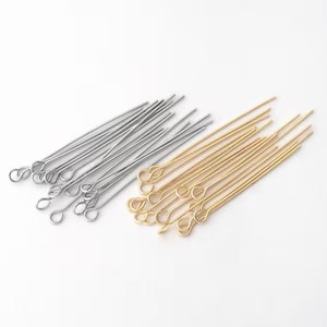 Puede incluir: Un conjunto de alfileres de ojo plateados y dorados, ideales para la fabricación de joyas y manualidades. Los alfileres están dispuestos en dos montones separados, con los plateados a la izquierda y los dorados a la derecha. Cada alfiler tiene un extremo en bucle.