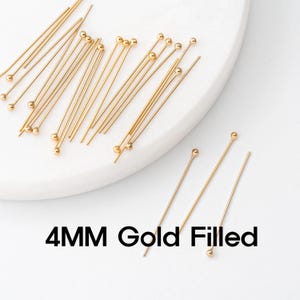 May include: Gold-filled head pins with a 4mm ball end. The pins are gold in color and are scattered on a white surface. The text "4MM Gold Filled" is displayed in black.