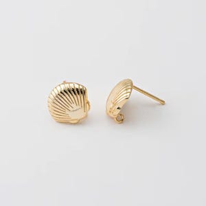 May include: A pair of gold-colored seashell stud earrings. The earrings are round with a ridged texture, resembling a scallop shell. The posts are straight and the earrings are set against a white background.