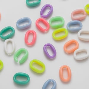 Könnte beinhalten: Eine Ansammlung farbenfroher, oval geformter Kunststoffglieder in verschiedenen Farbtönen wie Rosa, Grün, Lila, Gelb und Blau. Die Glieder sind auf einer weißen Oberfläche verstreut, einige offen und einige geschlossen, was darauf hindeutet, dass sie verbunden werden können.