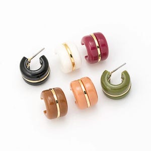 Op de afbeelding: Zes dikke oorringen in verschillende kleuren: zwart, wit, bordeaux, bruin, perzik en olijfgroen. Elke oorring heeft een goudkleurige band. De oorbellen worden op een witte ondergrond gepresenteerd.