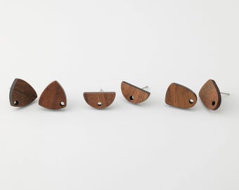 May include: Six wooden stud earrings in various geometric shapes. The earrings are made of dark brown wood and have a small hole near the bottom. Each earring has a silver post for piercing.
