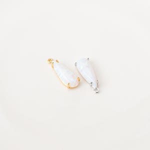 May include: Two teardrop-shaped pendants featuring iridescent white stones. One pendant is set in a gold-toned metal frame with a small loop at the top, while the other is set in a silver-toned metal frame with a matching loop at the top.