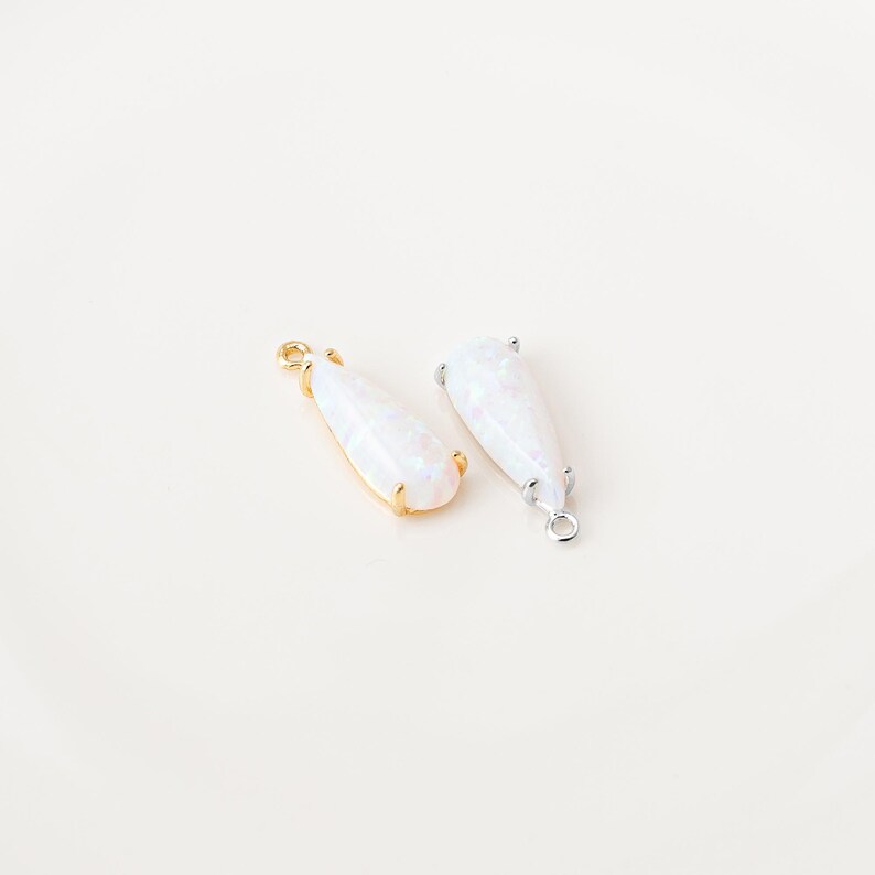 May include: Two teardrop-shaped pendants featuring iridescent white stones. One pendant is set in a gold-toned metal frame with a small loop at the top, while the other is set in a silver-toned metal frame with a matching loop at the top.