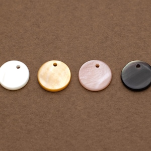 May include: Four circular pendants in a row, each with a small hole for threading. The pendants are white, gold, pink, and black. These pendants are likely for jewellery making or crafts.