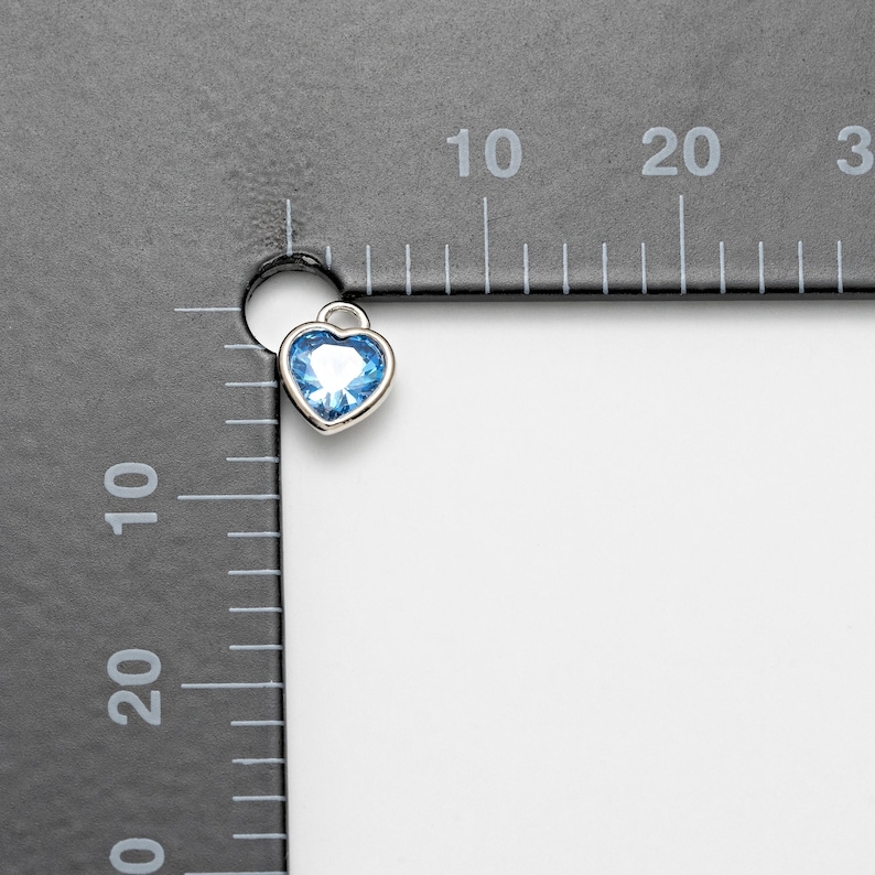 May include: A silver heart charm with a light blue crystal in the center. The charm is about 1 cm in size.