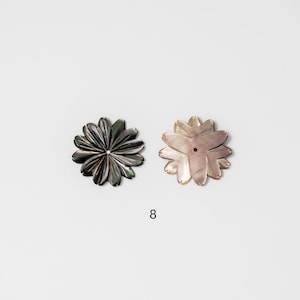 Puede incluir: Dos objetos decorativos con forma de flor. Uno es gris oscuro con brillo met&aacute;lico, y el otro es rosa claro con acabado nacarado. Ambos tienen un agujero central. El n&uacute;mero "8" est&aacute; impreso en negro debajo.