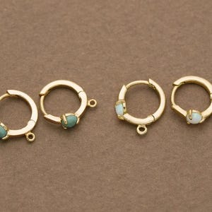 Op de afbeelding: Vier gouden creolen met elk een klein edelsteentje. Twee oorbellen hebben een turquoise edelsteentje en twee oorbellen hebben een wit opaal steentje.
