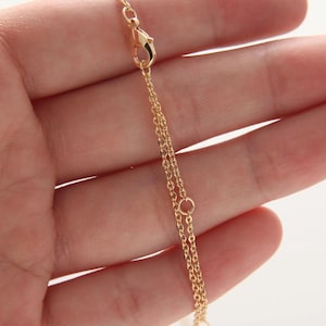 Könnte beinhalten: Eine goldene Kettenkette mit einem Karabinerverschluss und einem kleinen runden Ring.