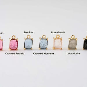 May include: Eight gold-toned charms with different colored glass stones. The stones are labeled "Fuchsia", "Montana", "Rose Quartz", "Jet", "Cracked Fuchsia", "Cracked Montana", "Labradorite", and "Jet".