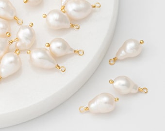May include: A collection of teardrop-shaped, off-white pearls with gold-colored wire loops. The pearls have a lustrous, smooth surface and are arranged on a white surface. These are ideal for jewelry making.