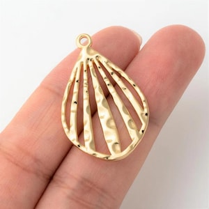 May include: A gold-colored, teardrop-shaped pendant with a textured surface and a series of vertical bars. The pendant has a small loop at the top for attaching to a chain or other jewelry component. The design is open and airy.