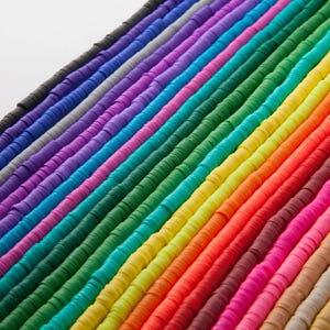 May include: Rows of colorful, flat disc beads in a rainbow of hues. The beads are arranged diagonally, showcasing a spectrum of colors from black to beige. The beads are uniform in size and shape, ideal for jewelry making and crafting.