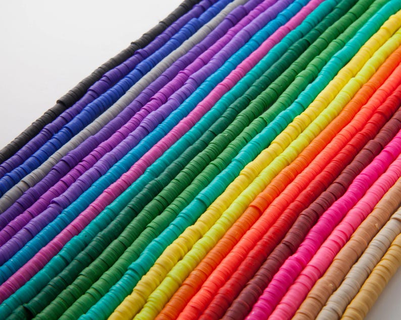 May include: Rows of colorful, flat disc beads in a rainbow of hues. The beads are arranged diagonally, showcasing a spectrum of colors from black to beige. The beads are uniform in size and shape, ideal for jewelry making and crafting.