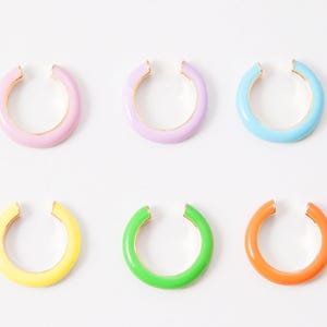 Puede incluir: Seis pendientes de aro de colores en varios colores, incluyendo rosa, azul claro, amarillo, verde y naranja. Los pendientes de aro están hechos de metal y tienen un diseño simple y abierto.