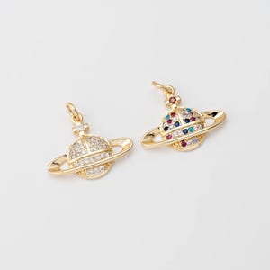 May include: Two gold-colored planet-shaped pendants. One pendant is encrusted with clear crystals, while the other features a colorful array of gemstones. Both have a small loop at the top for hanging.