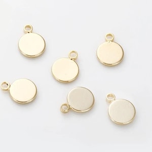 Op de afbeelding: Verschillende goudkleurige, ronde bedels met een kleine lus aan de bovenkant om aan sieraden te bevestigen. De bedels zijn glad en glanzend, met een eenvoudig, minimalistisch ontwerp. Ze liggen op een witte achtergrond.