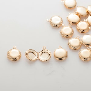 Op de afbeelding: Een verzameling gouden metalen medaillonbedels met ingewikkelde ontwerpen. De medaillons zijn rond en hebben een scharnierende opening.