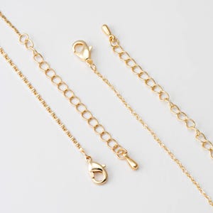 Puede incluir: Primer plano de varios extensores y cadenas de collar dorados. Los extensores tienen cierres de mosquetón y pequeños eslabones de cadena. Las cadenas varían en estilo, algunas con eslabones delicados y otras con eslabones más grandes.